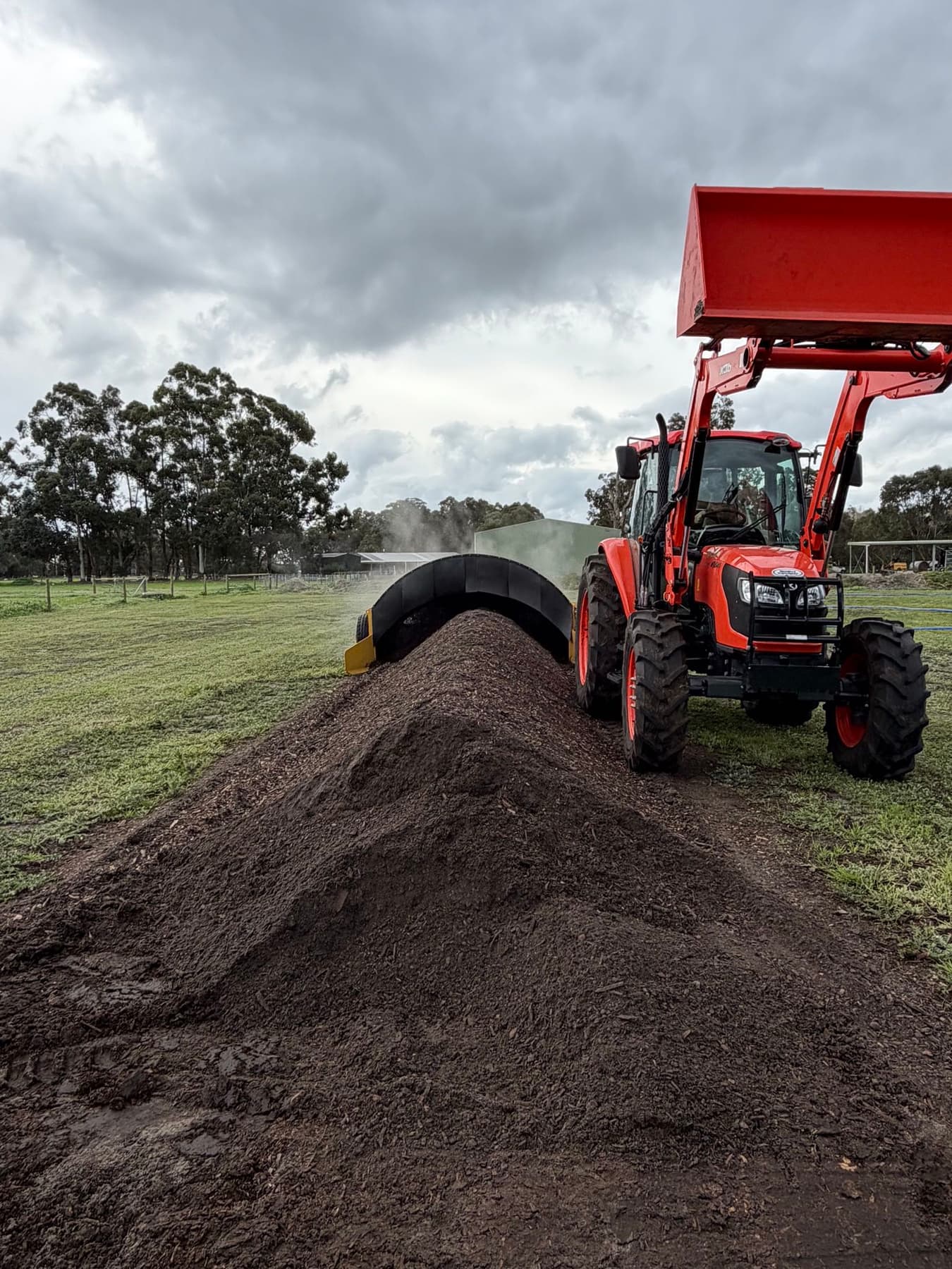 Tractor turning a steaming compost windrow at the WildSoil site